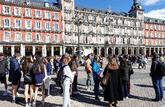 Eine Schüler*innengruppe steht auf der Plaza Mayor in Madrid. Rundherum sind rote, mehrstöckige Gebäude mit Arkaden, der Platz ist gut besucht.