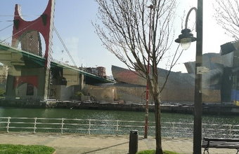 Blick auf den Fluss Nervión in Bilbao mit der markanten roten Brücke und dem Guggenheim-Museum im Hintergrund.
