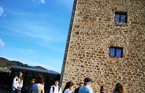 Eine Gruppe Jugendlicher steht auf einer Wiese vor einem hohen, historischen Steingebäude. Der Himmel ist blau.